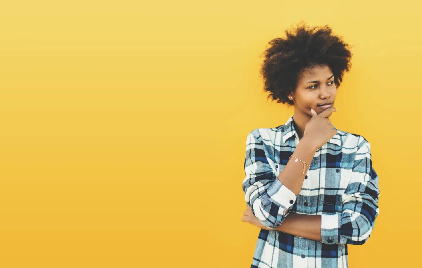 young woman thinking in front of a yellow wall