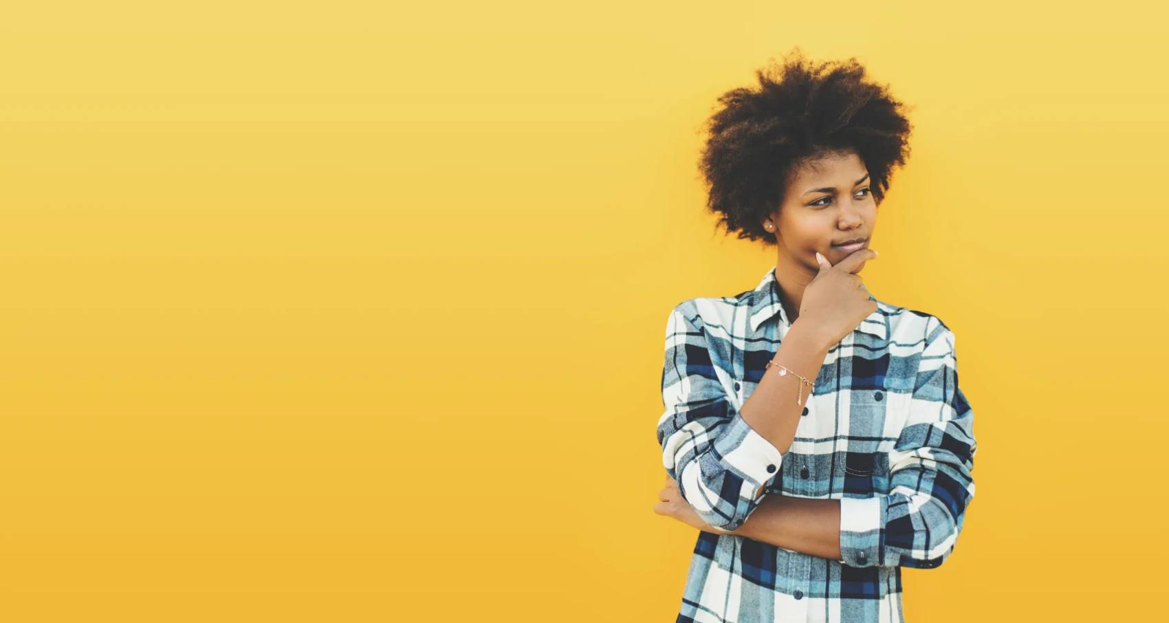 young woman thinking in front of a yellow wall