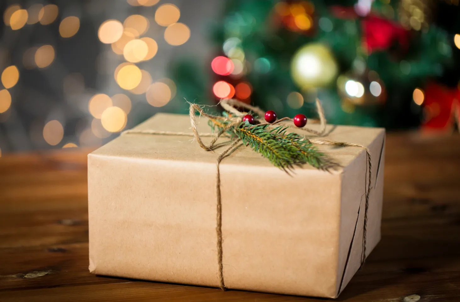 present wrapped in simple brown paper with lit tree in the background